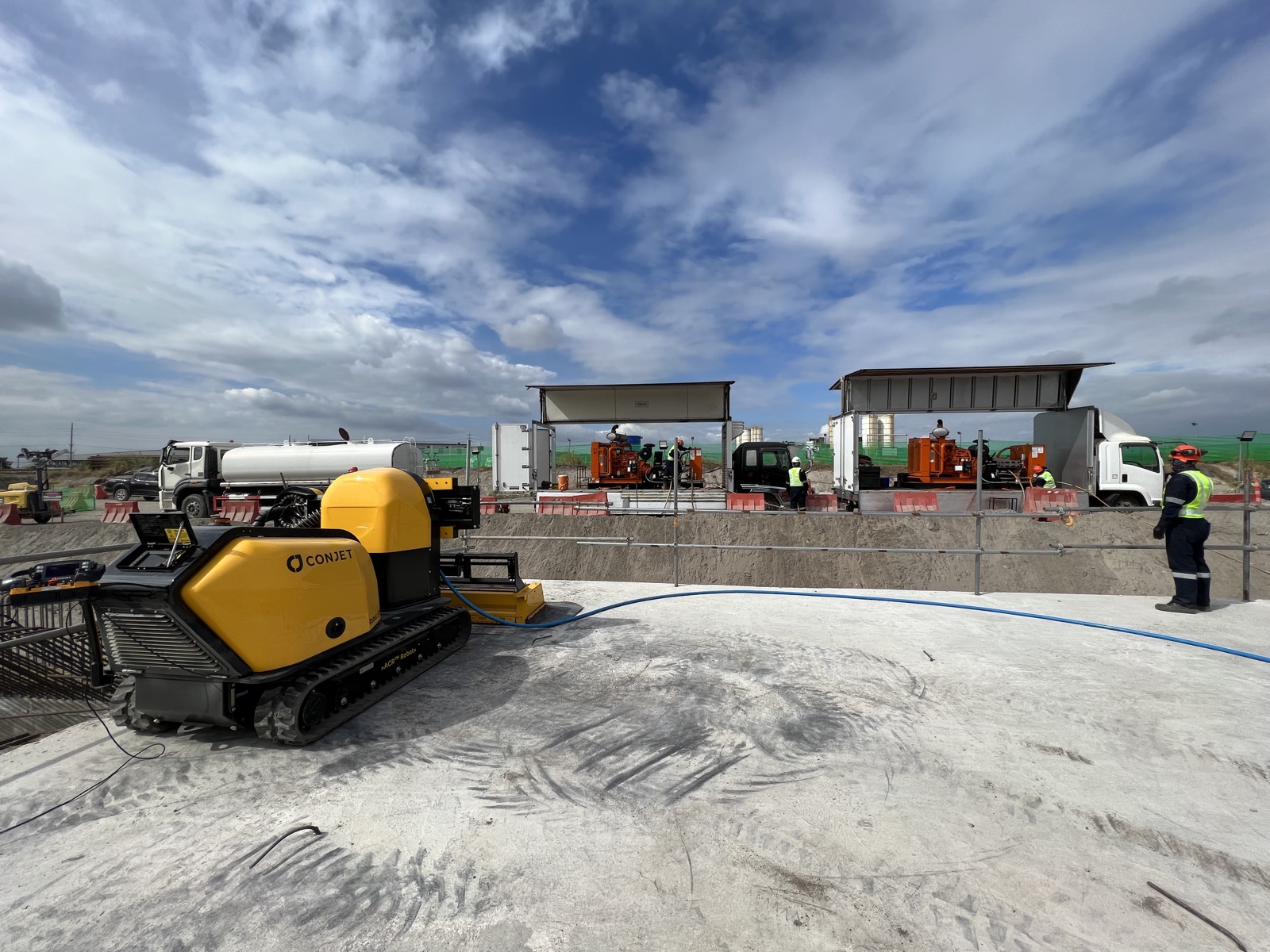 Conjet ACR hydrodemolition robot positioned on the concrete structure with two truck-mounted NLB ultra high pressure pump units and Dezu crew behind it on the railway project site