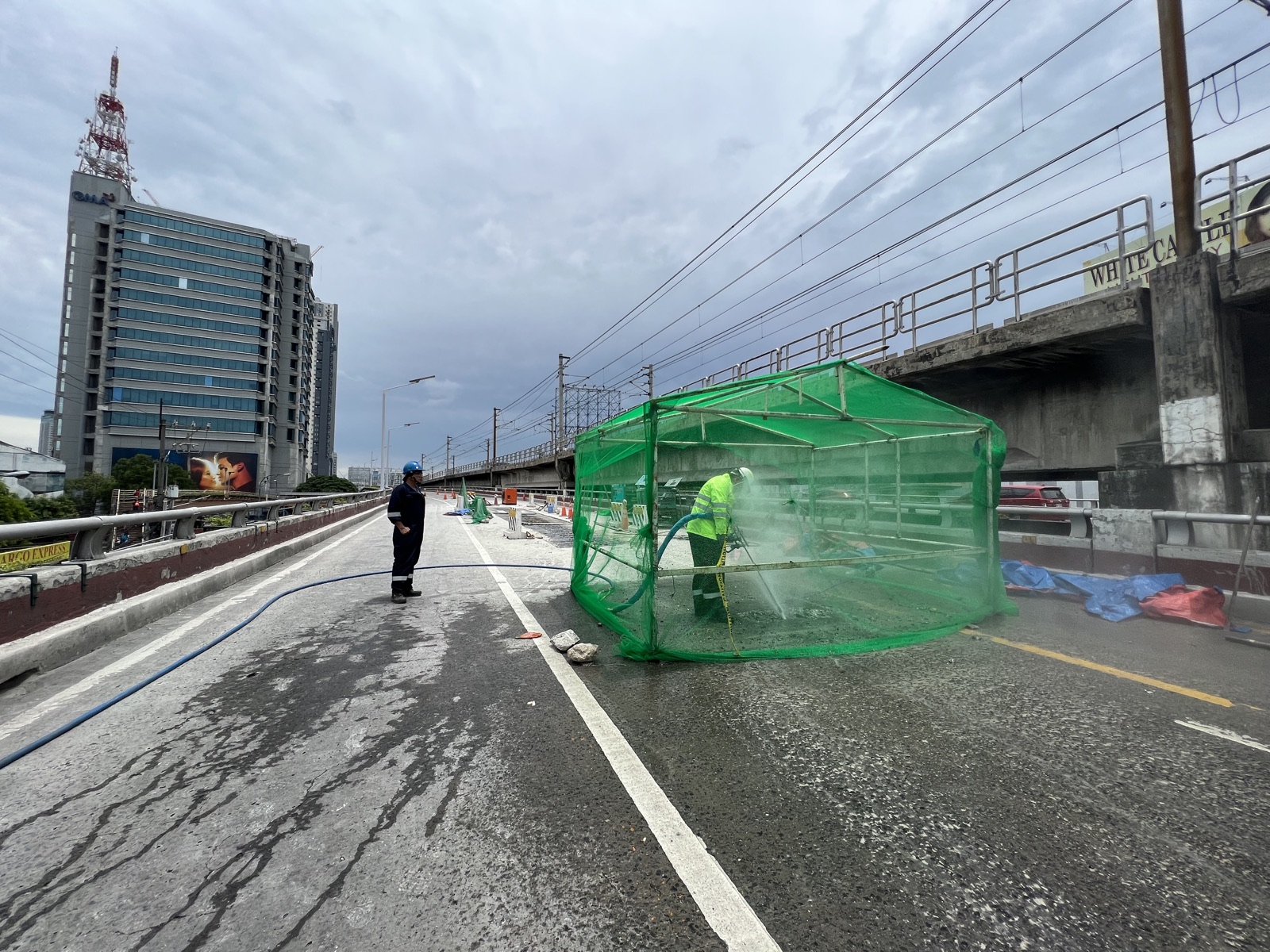 Dezu operator performing high pressure water jetting inside a green containment enclosure on the EDSA busway, Metro Manila, with supervisor observing