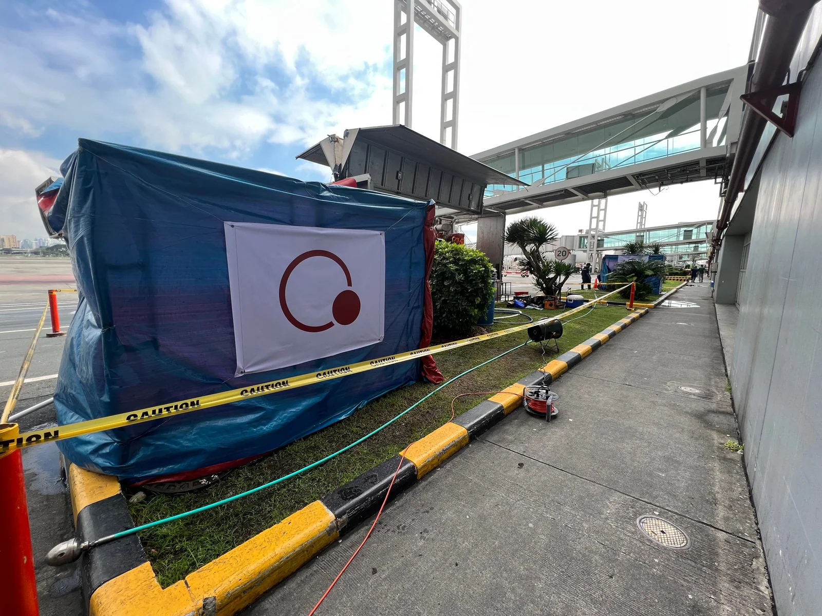 Dezu work-area enclosure, barriers and hoses beside an airport terminal during drainage cleaning